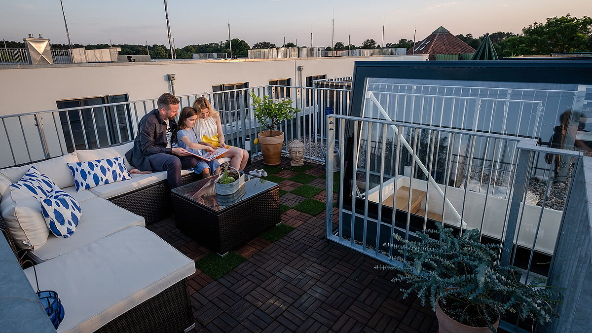 Eine Familie sitzt bei Sonnenuntergang auf der gemütlichen Dachterrasse mit Sitzbereich von ihrem Townhouse in Berlin mit Flachdach Ausstieg.