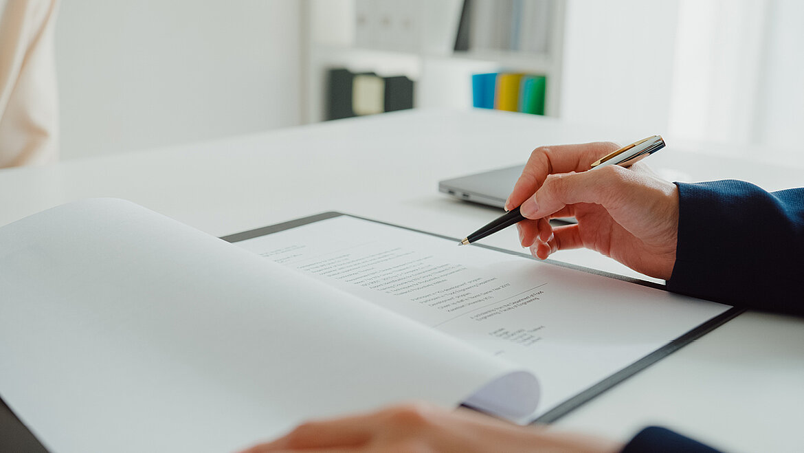 Hand mit Stift unterschreibt Vertrag am Schreibtisch im Büro