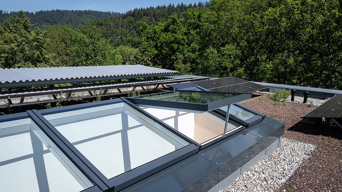 Wohnhaus in Freiburg mit einem modularen Glasdach von LAMILUX, teilweise geöffnet, umgeben von Solarpanels und begrüntem Flachdach.