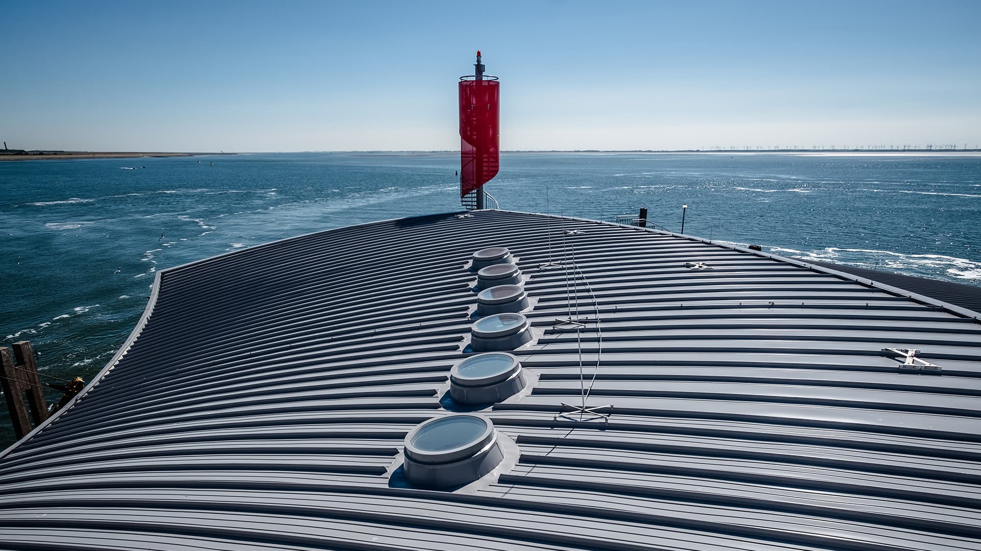 Dach des Hafenterminals Norderney mit runden Oberlichtern, die Tageslicht einlassen, vor der Kulisse des Meeres.